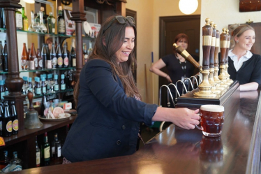 Nicola pulling a pint behind a bar